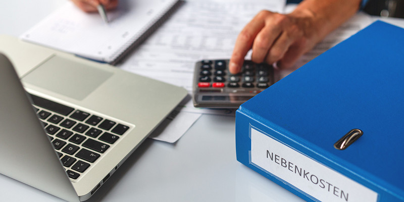 Mann tippt auf Taschenrechner neben Ordner mit Nebenkosten
