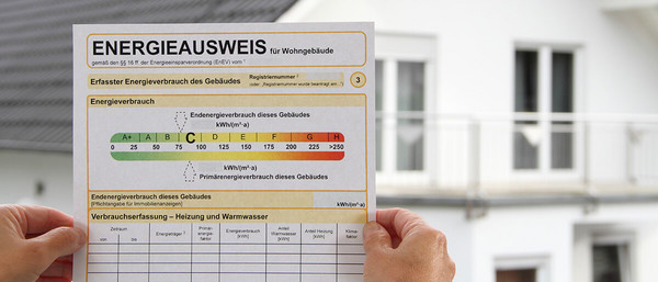 Mann hält Energieausweis in den Händen vor Haus