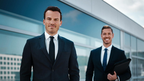 Zwei erfahrene Makler stehen nebeneinander und schauen lachend in die Kamera