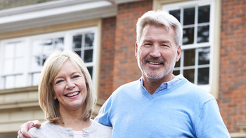 Glückliches Ehepaar steht vor einem Haus und lächelt in die Kamera