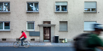 Altes Haus von aussen und Radfahrer fahren auf der Strasse vorne durch