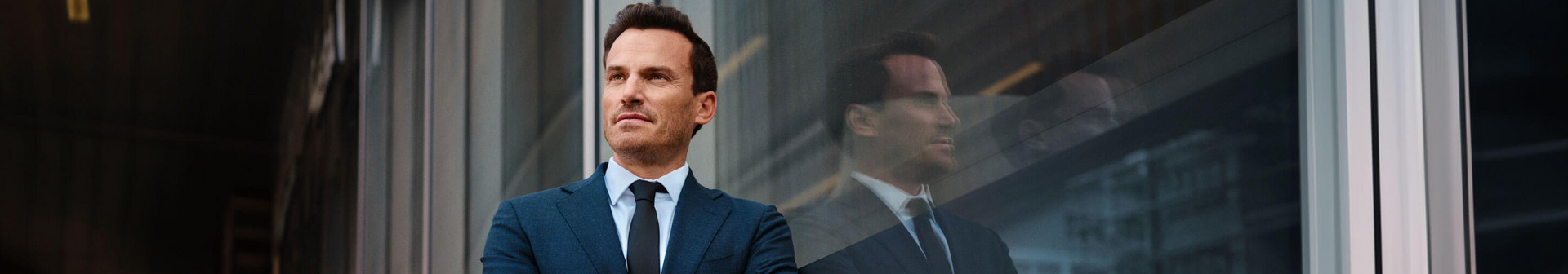 Makler schaut an der Kamera vorbei mit Haus im Hintergrund