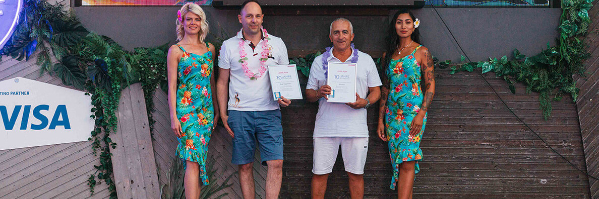 Männer halten Urkunde auf Foto mit Hostessen im Hawaii Kleid