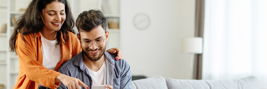 Junges Paar sitzt auf beiger Couch und lächelt