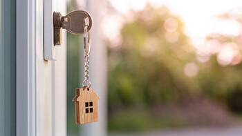 Schlüsselanhänger mit einem kleinem Haus hängt an Schlüssel, der in der Türe steckt