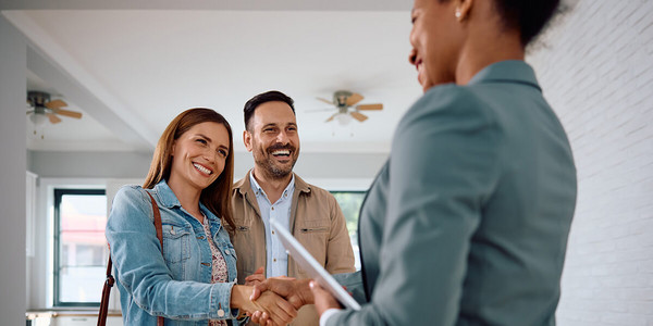 Paar in Wohnung lacht und schüttelt Frau die Hand
