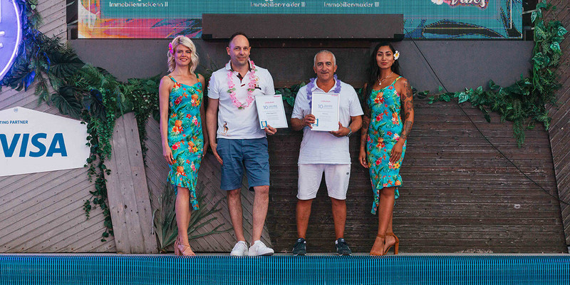 Männer halten Urkunde auf Foto mit Hostessen im Hawaii Kleid