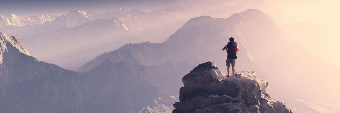 Mann steht mit Rucksack auf einem Berg