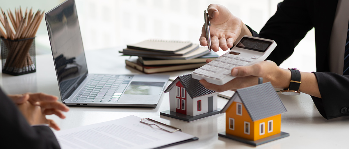 Person hält Taschenrechner neben Modellhäusern